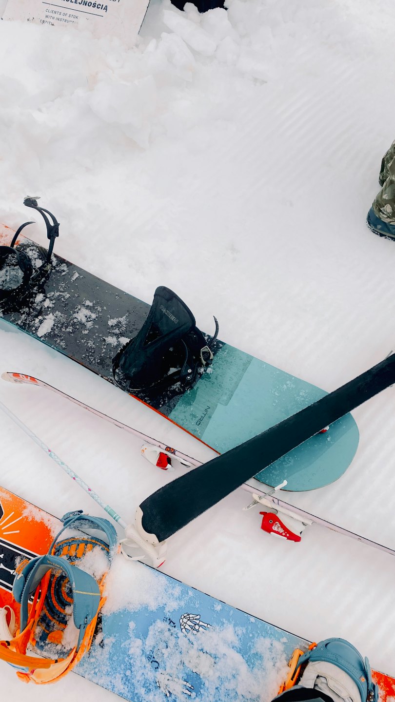 Snowboard e sci appoggiati su un pendio innevato battuto.