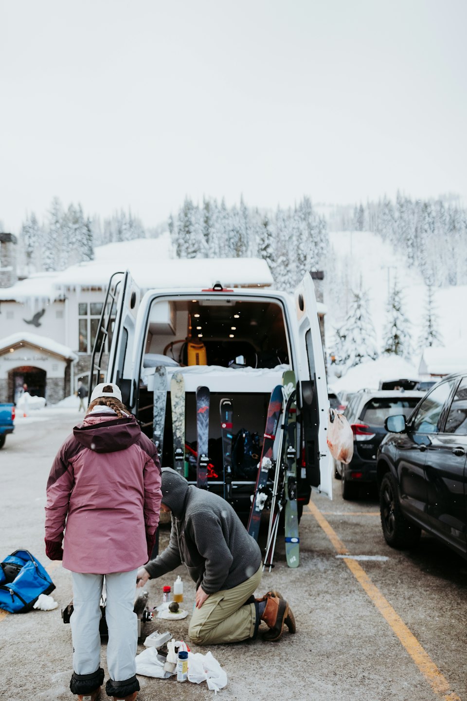 Persone preparano sci vicino a un furgone in un resort innevato.